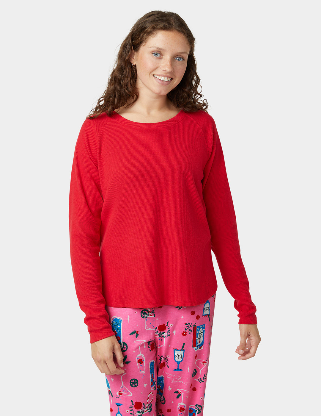 Person wearing a red long-sleeve top and pink pajama pants with a pattern on a white background