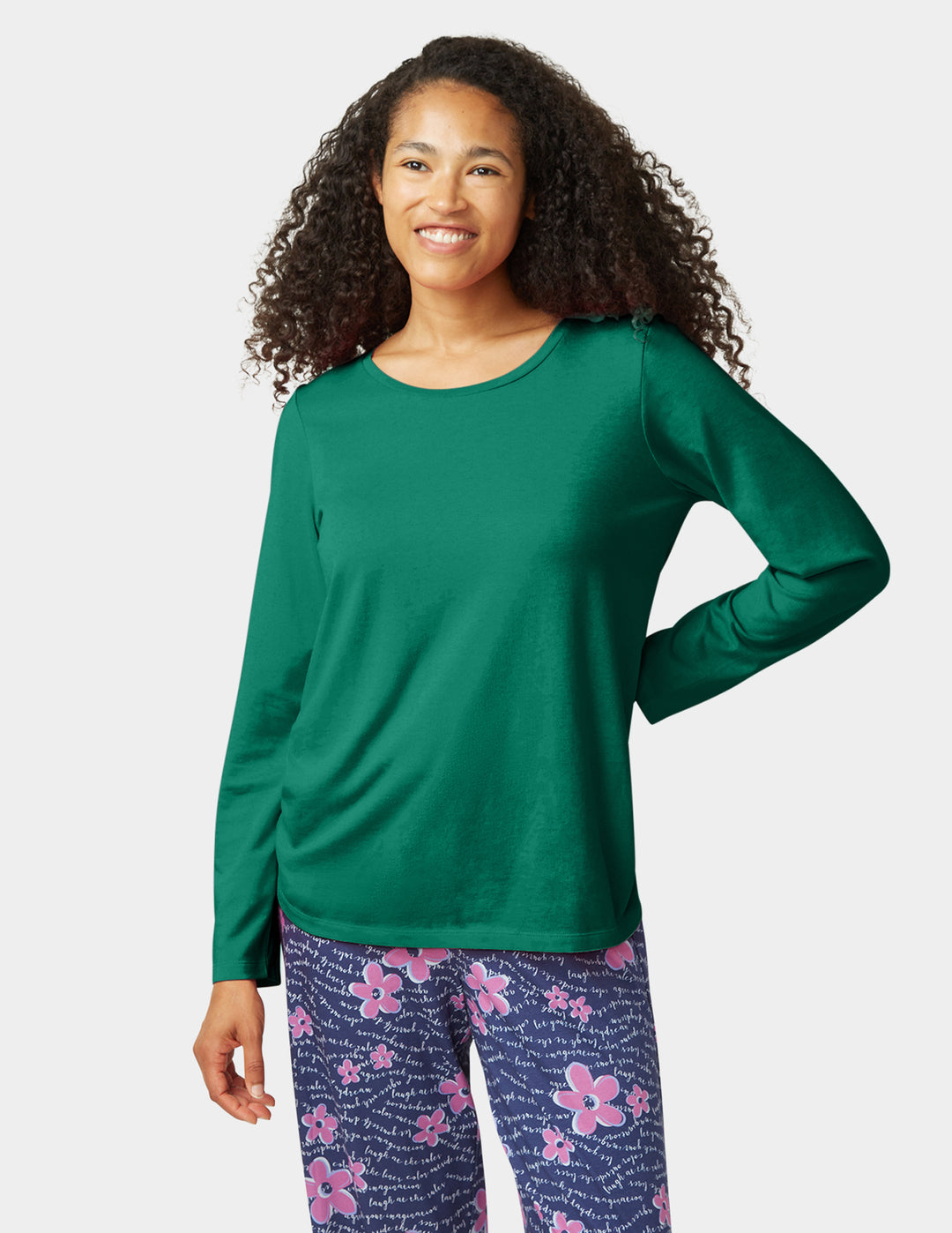 Woman wearing a green long-sleeve top and floral pants on a white background