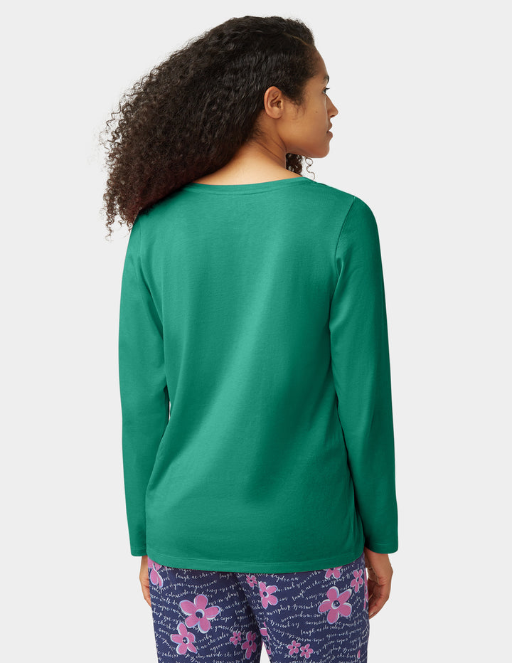 Person wearing a green long-sleeve shirt and floral pants on a white background