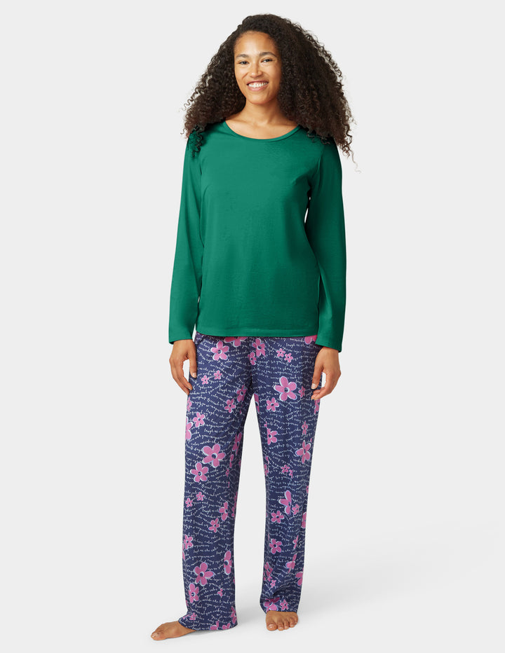 Woman wearing a green long-sleeve top and purple floral pants on a white background