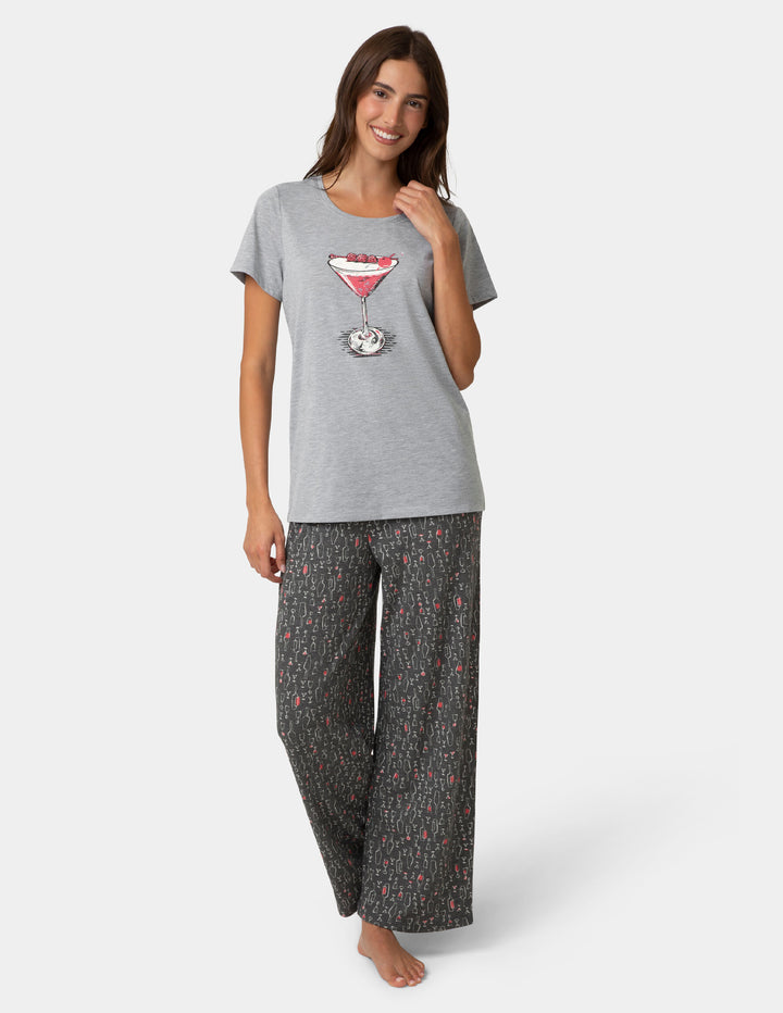 Woman wearing a gray t-shirt with a martini glass design and patterned pants on a white background