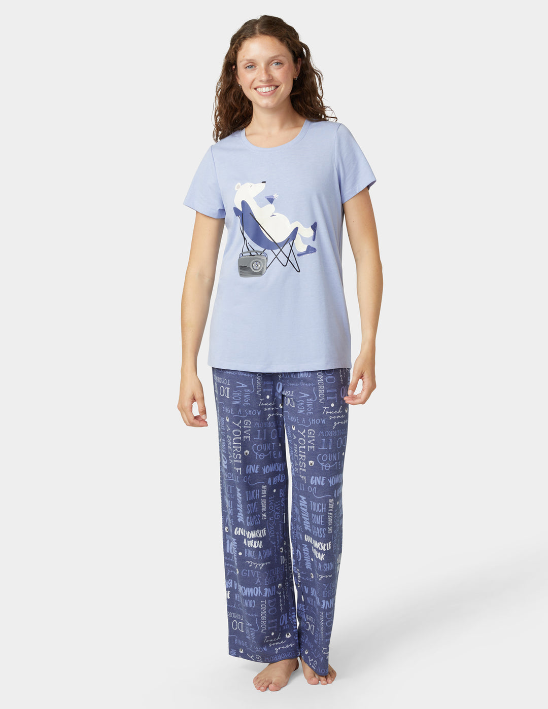 Woman wearing a light blue t-shirt with a graphic and dark blue patterned pants on a white background