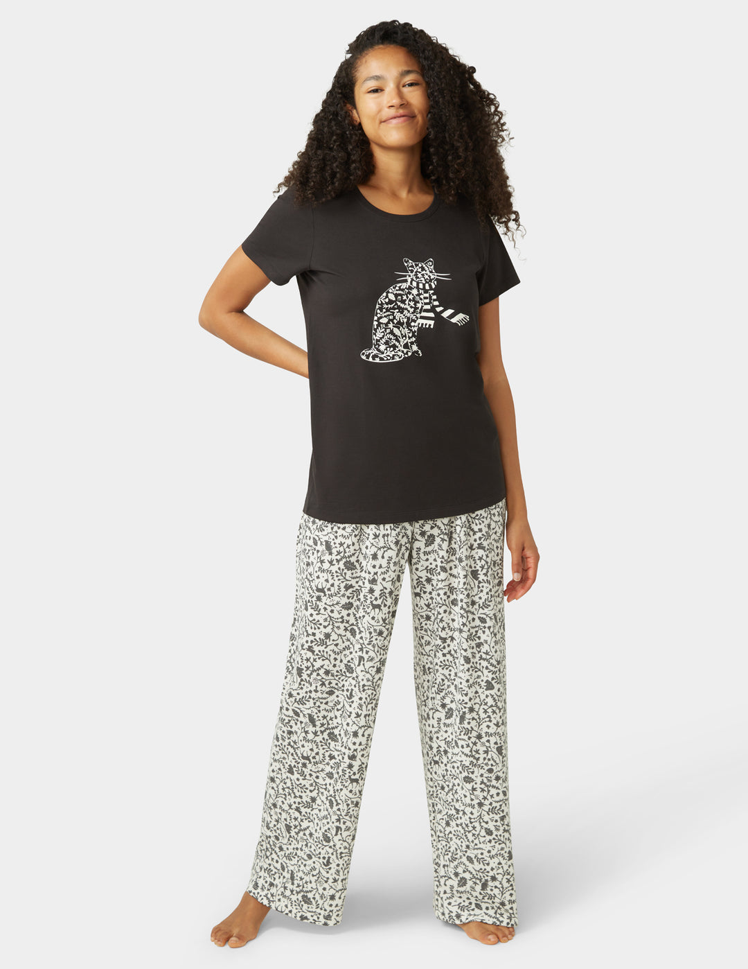 Woman wearing a black t-shirt with a white graphic and patterned pants on a white background