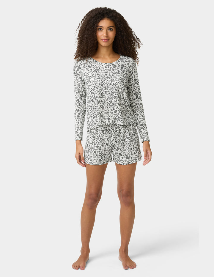 Woman wearing a long-sleeve pajama top and shorts set with a floral pattern on a white background