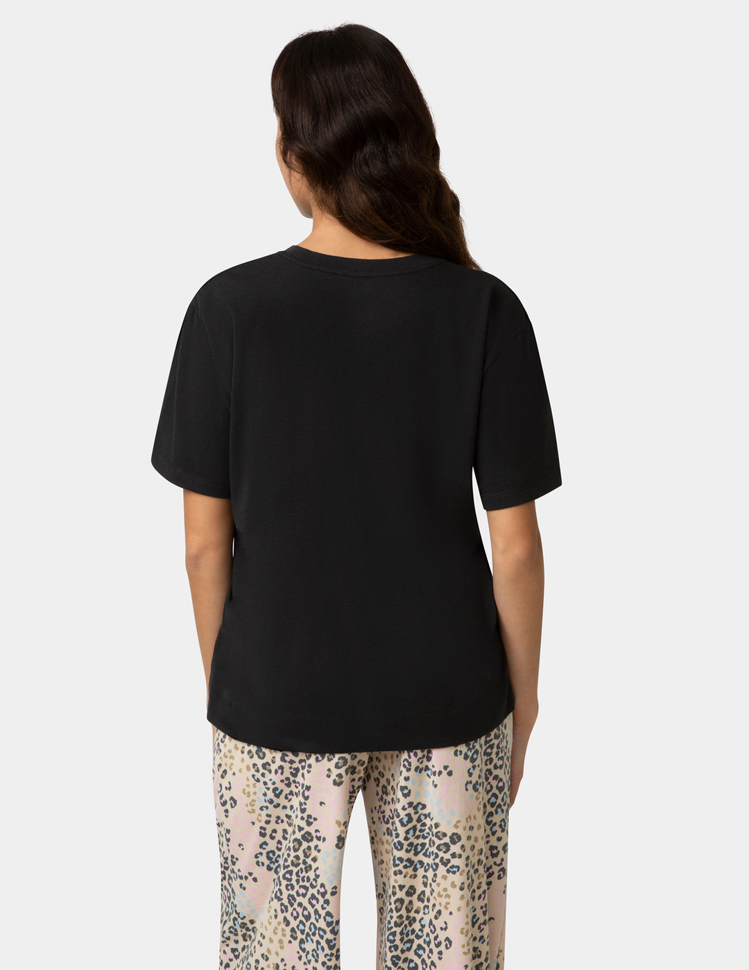 Person wearing a black t-shirt and patterned pants on a white background