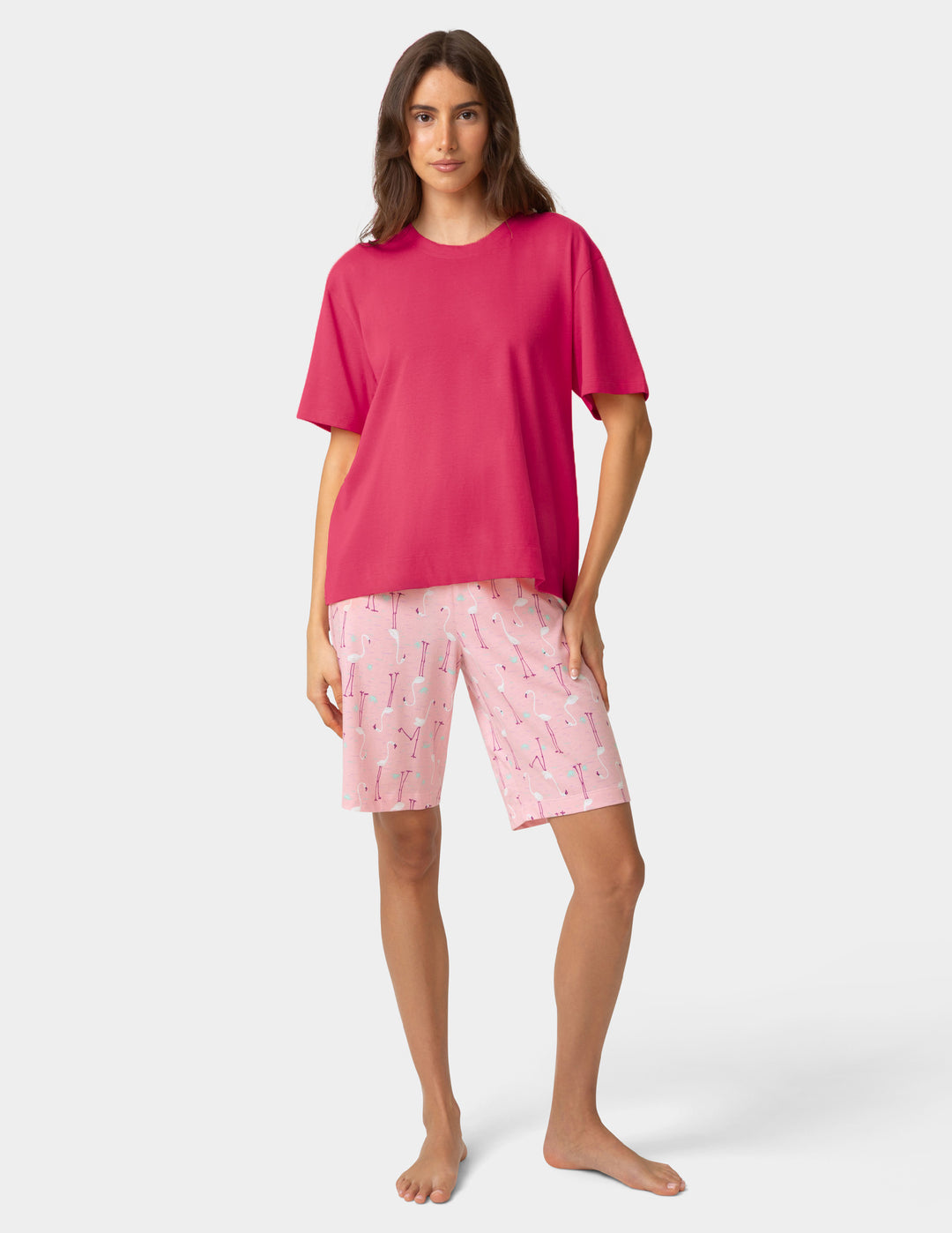 Woman wearing a pink pajama t-shirt and patterned shorts on a white background