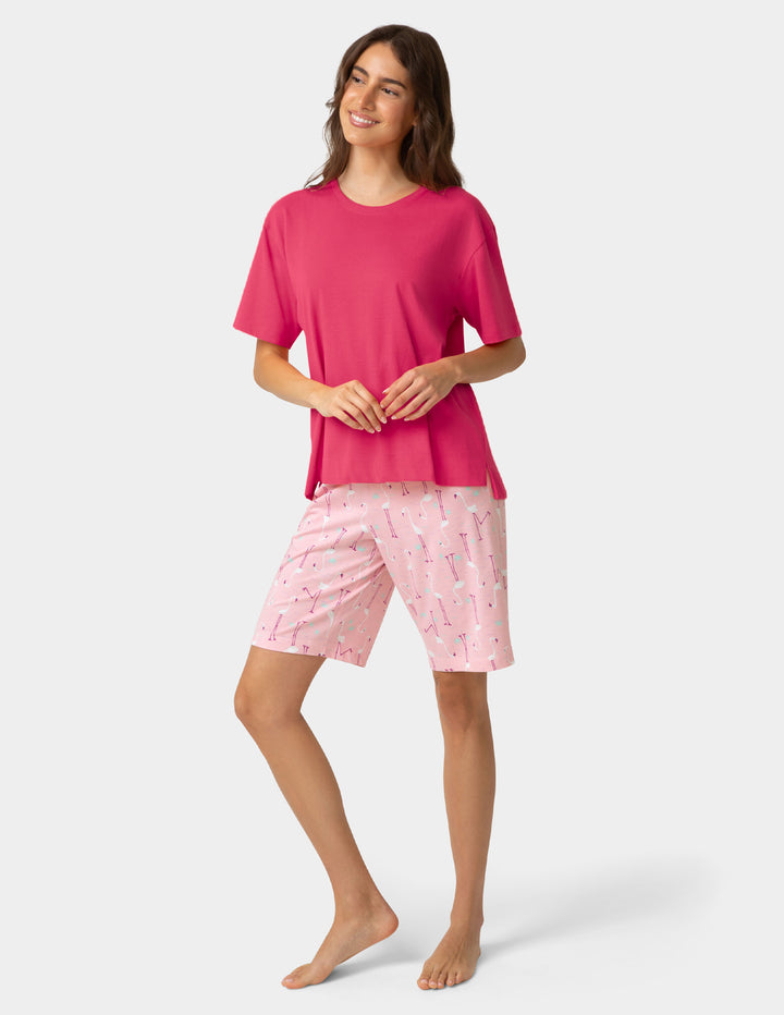 Woman wearing a dark pink pajama t-shirt and patterned shorts on a white background