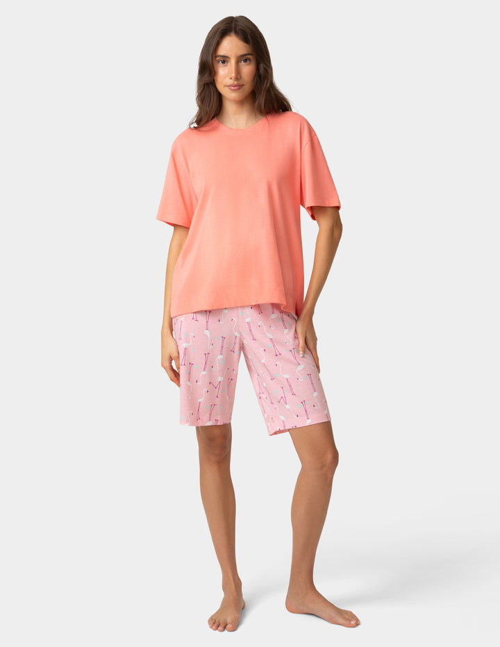 Woman wearing a coral t-shirt and pink patterned shorts on a white background