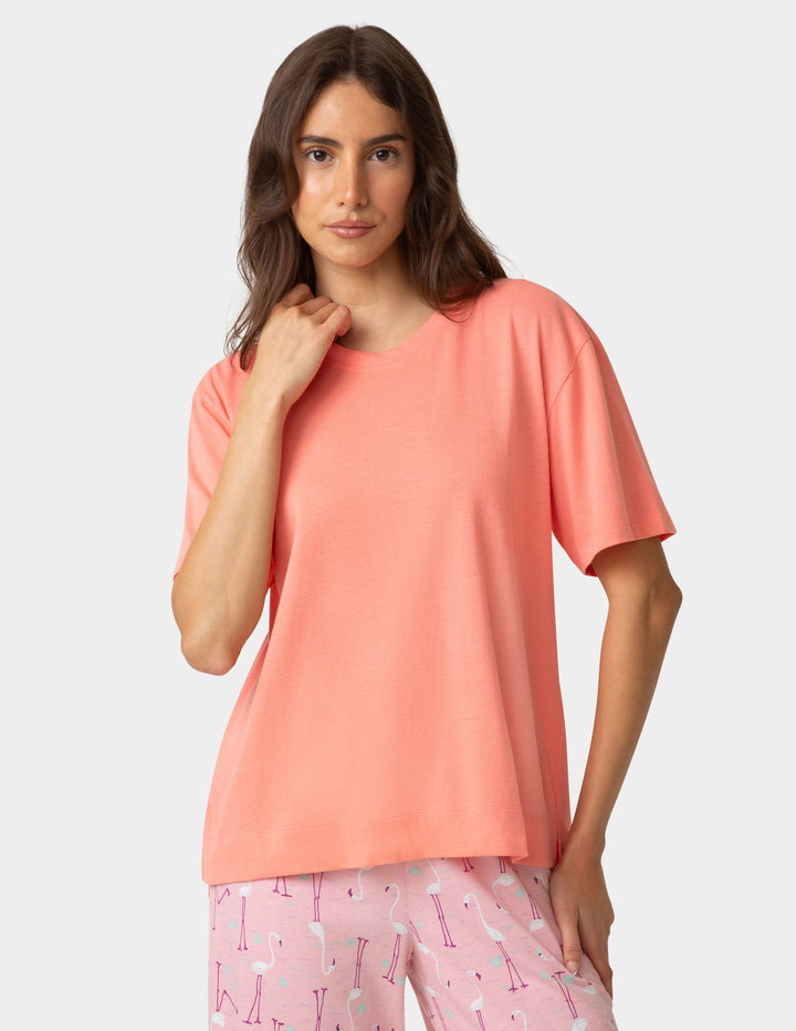 Woman wearing a coral top and pink pajama pants with a pattern on a light gray background