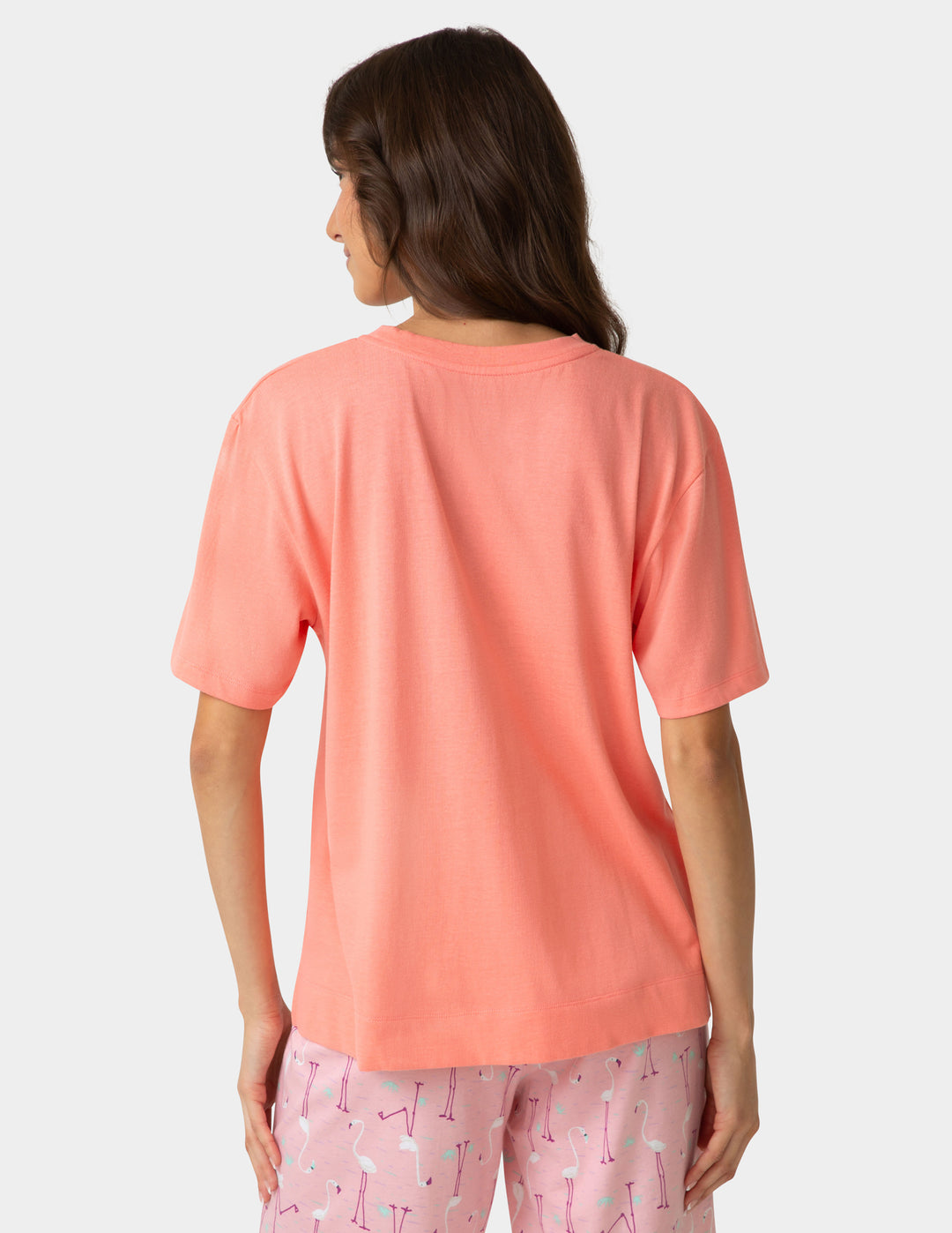 Woman wearing a coral t-shirt and pink pajama pants with flamingo pattern on a white background