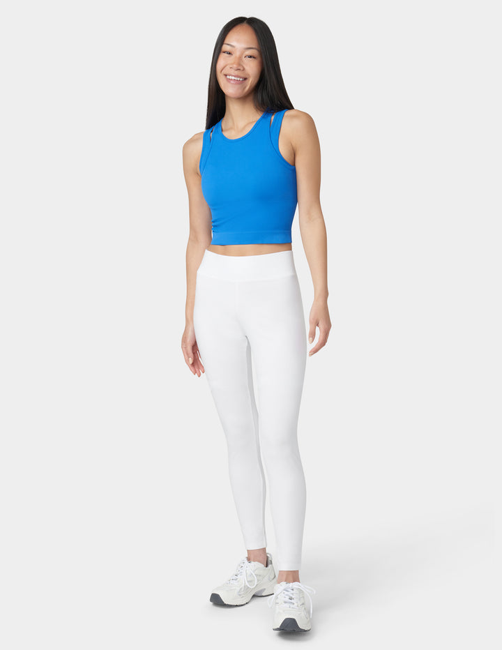 Woman wearing a blue athletic top and white leggings on a white background
