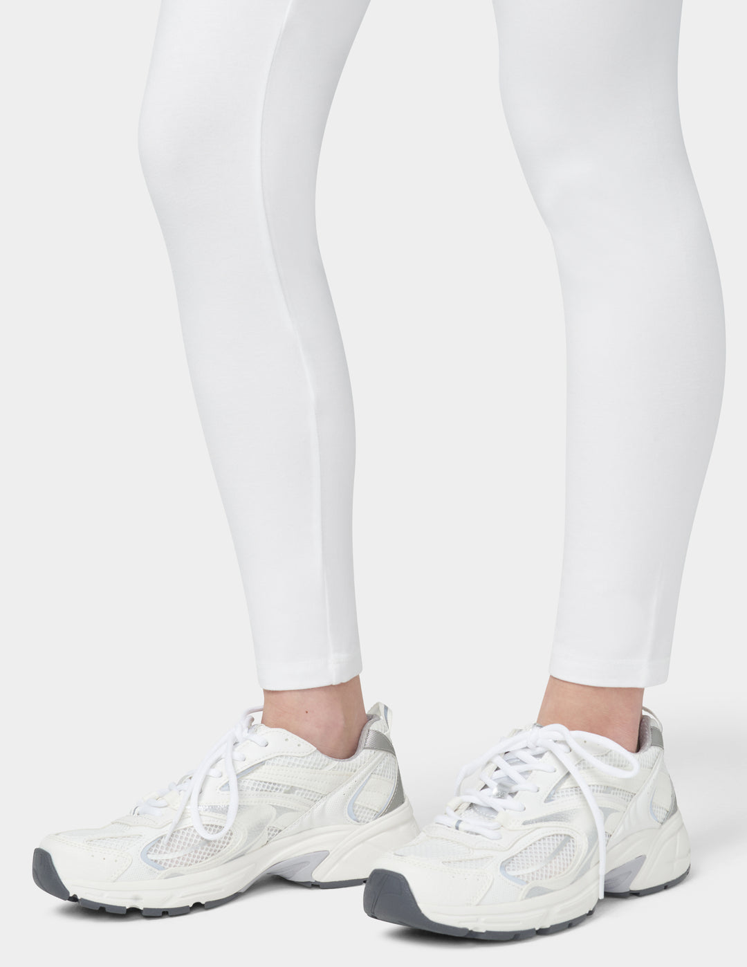 White sneakers worn with white leggings on a light gray background