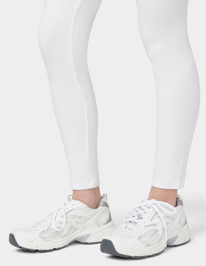 White sneakers worn with white leggings on a light gray background