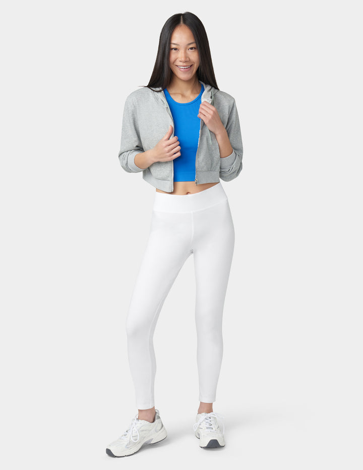 Woman wearing a gray jacket, blue top, white leggings, and white sneakers on a white background