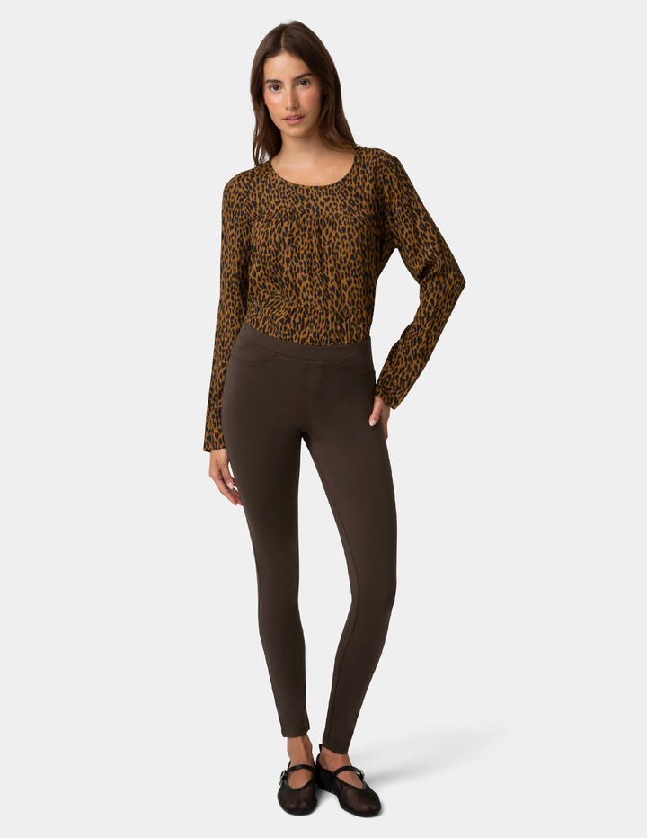Woman wearing a leopard print top and brown leggings on a white background