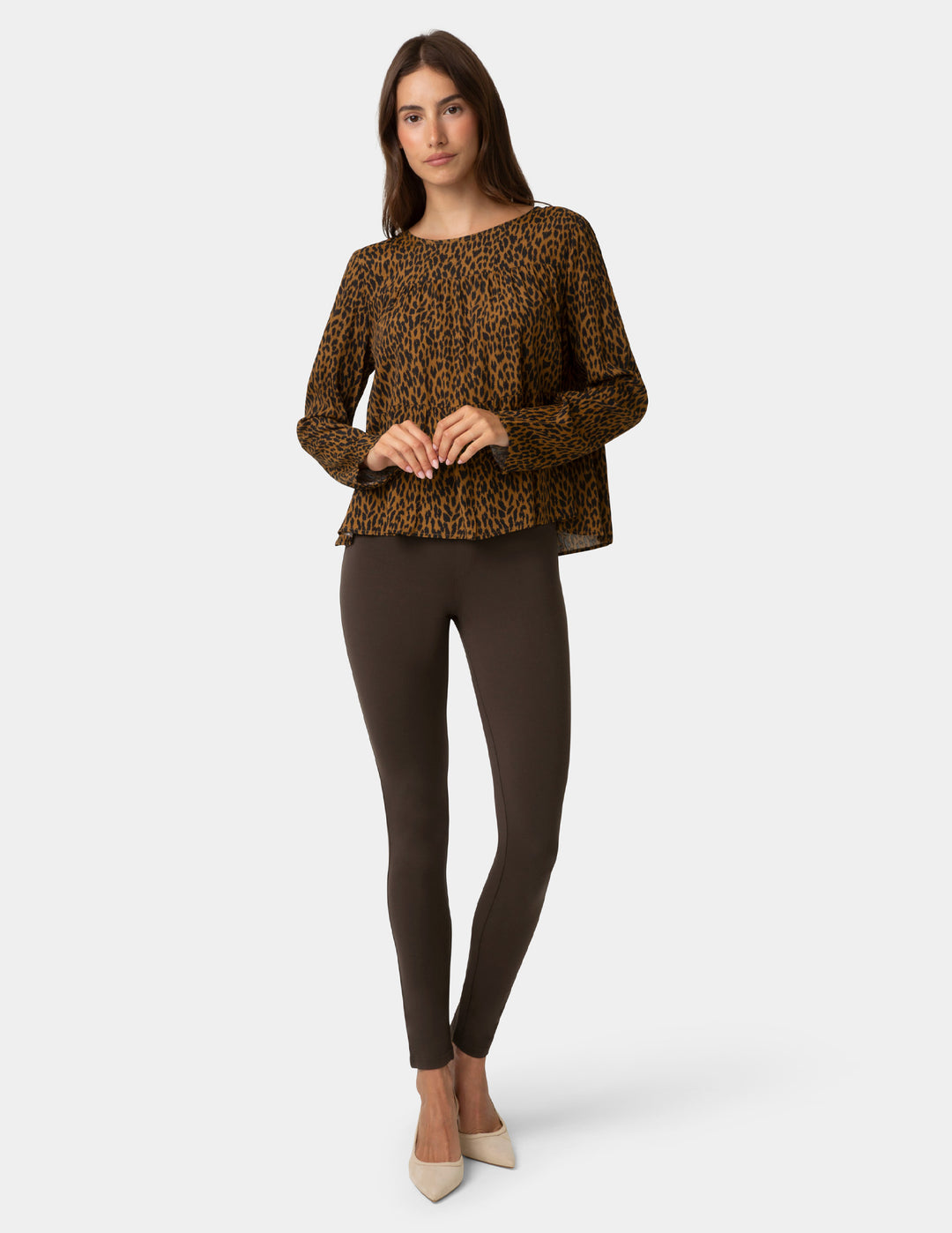 Woman wearing a leopard print top and dark brown leggings on a white background