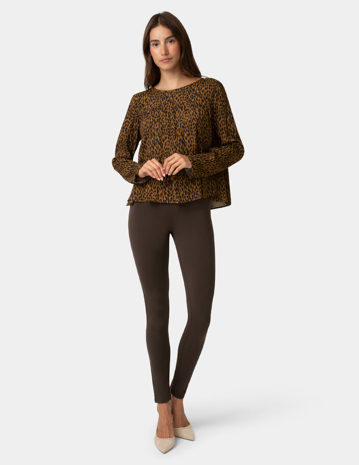 Woman wearing a leopard print top and dark brown leggings on a white background