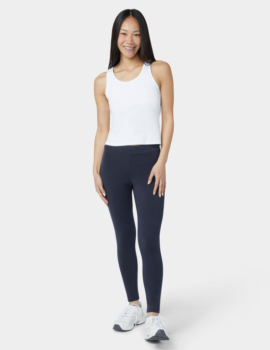 Woman wearing a white tank top and navy leggings on a white background