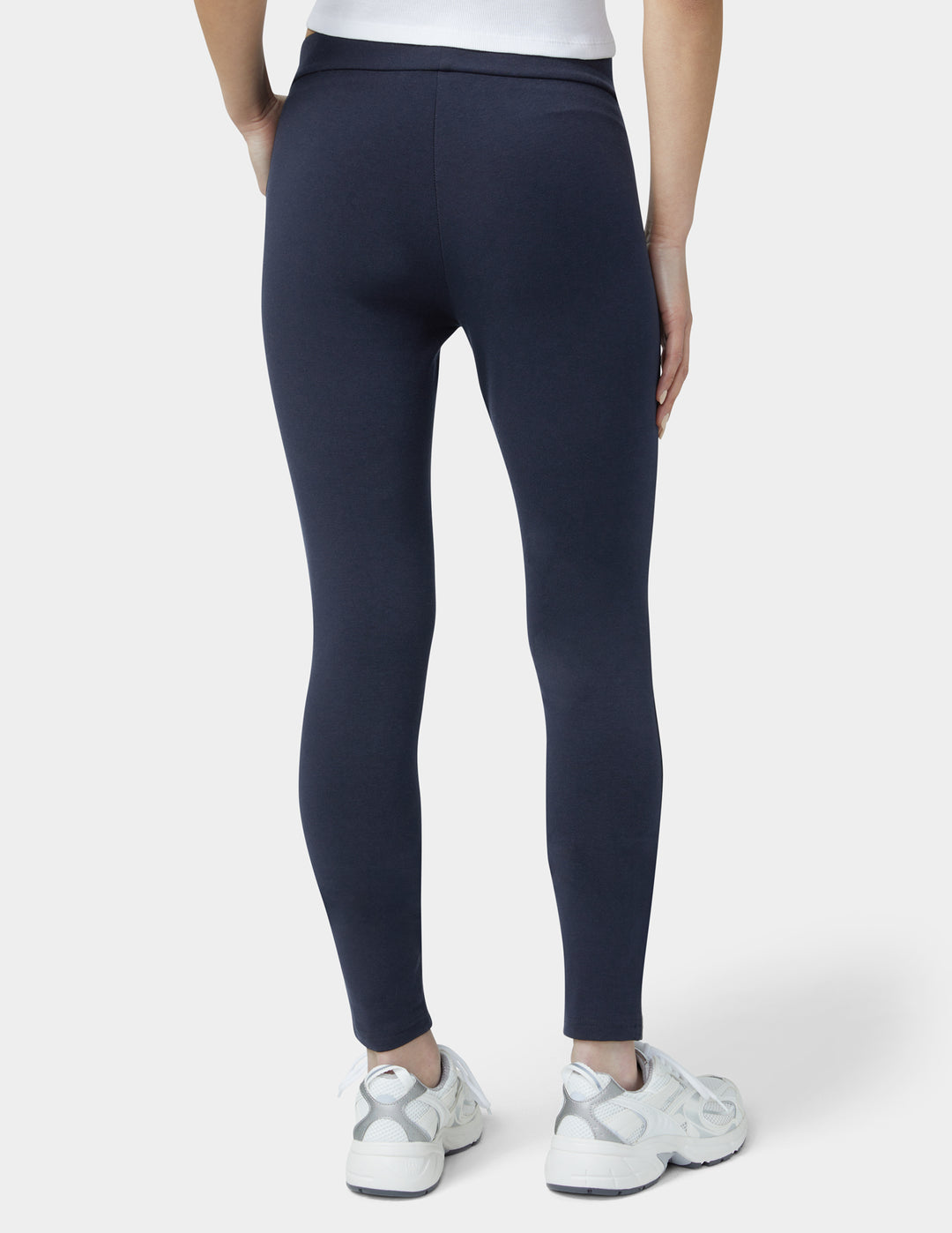 Person wearing navy leggings and white sneakers on a white background