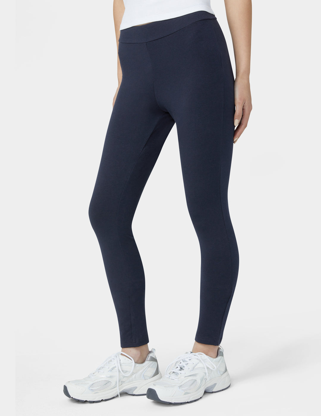 Person wearing navy leggings and white sneakers on a white background