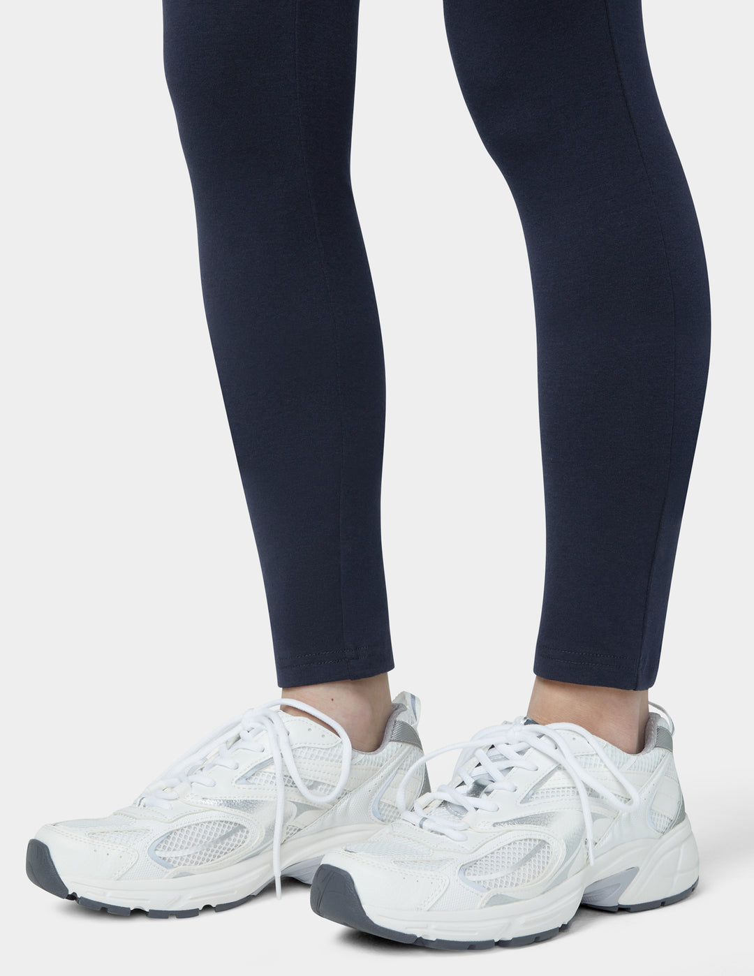 White sneakers worn with navy leggings on a white background