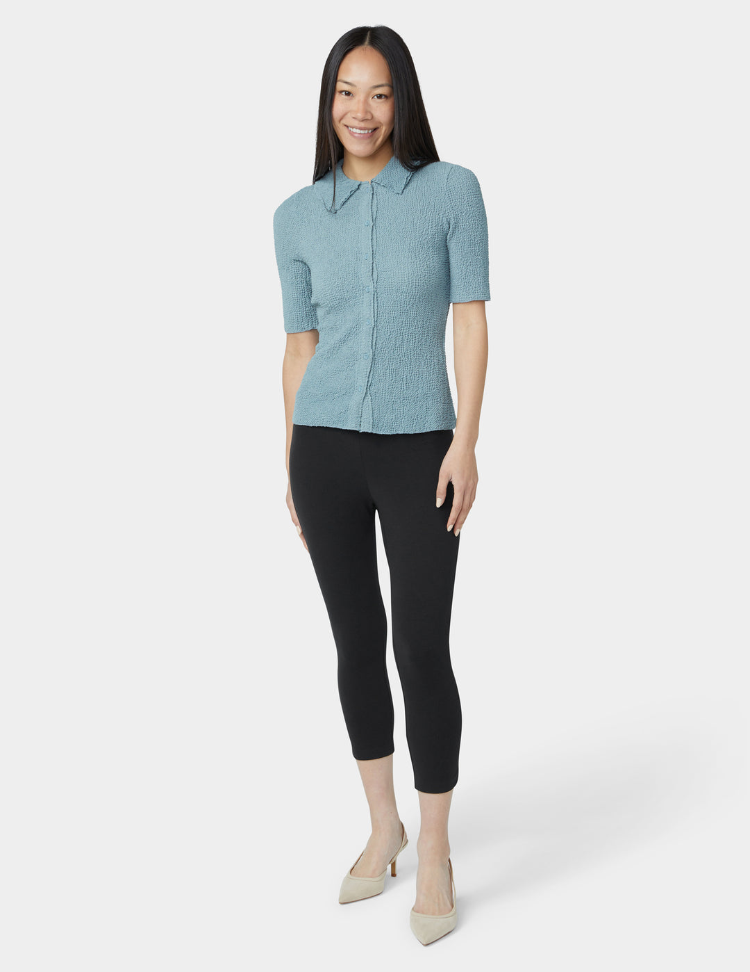 Woman wearing a light blue short-sleeve shirt and black pants on a white background