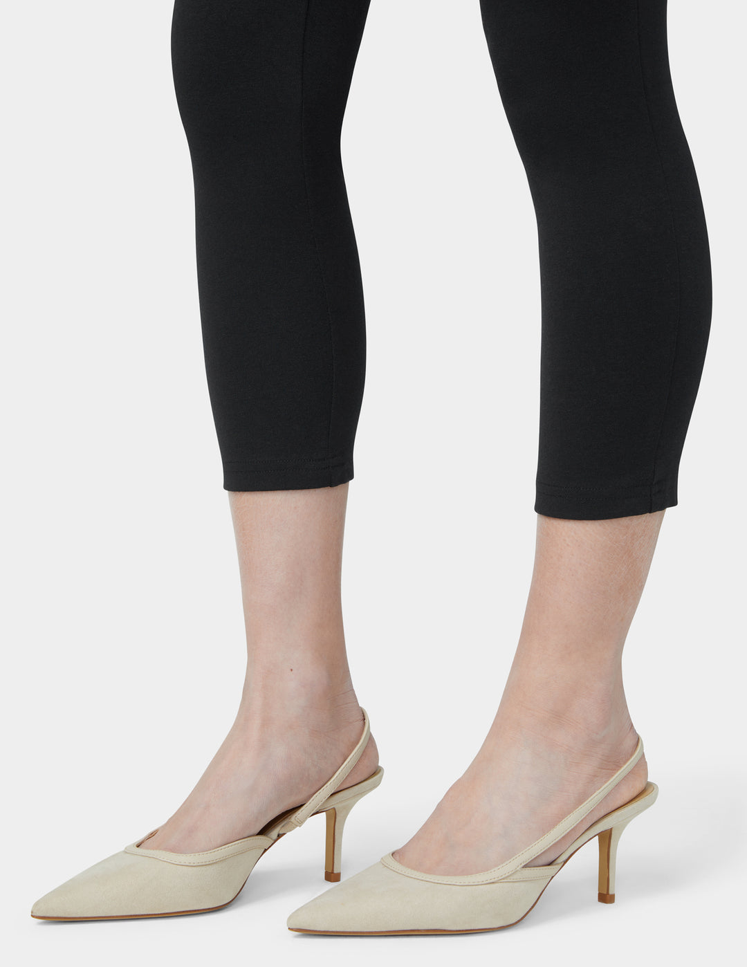 Beige high-heeled shoes worn with black leggings on a white background
