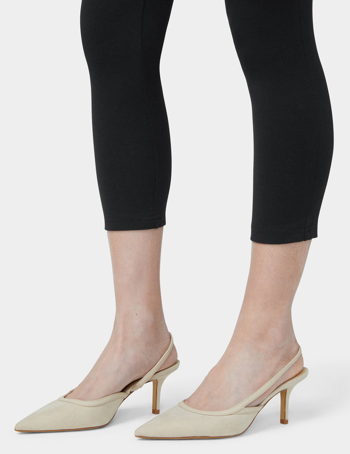 Beige high-heeled shoes worn with black leggings on a white background