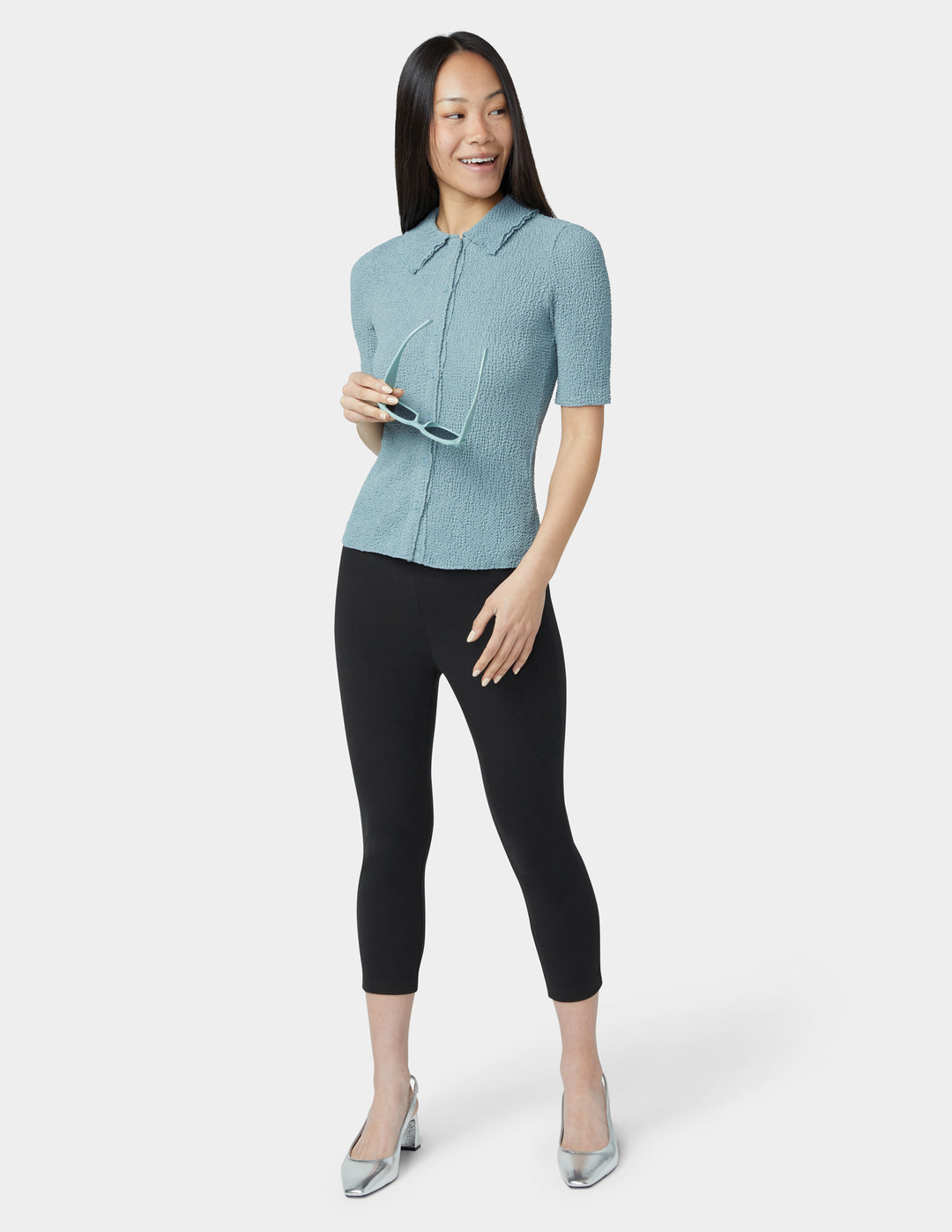 Woman wearing a light blue checkered blouse and black pants on a white background