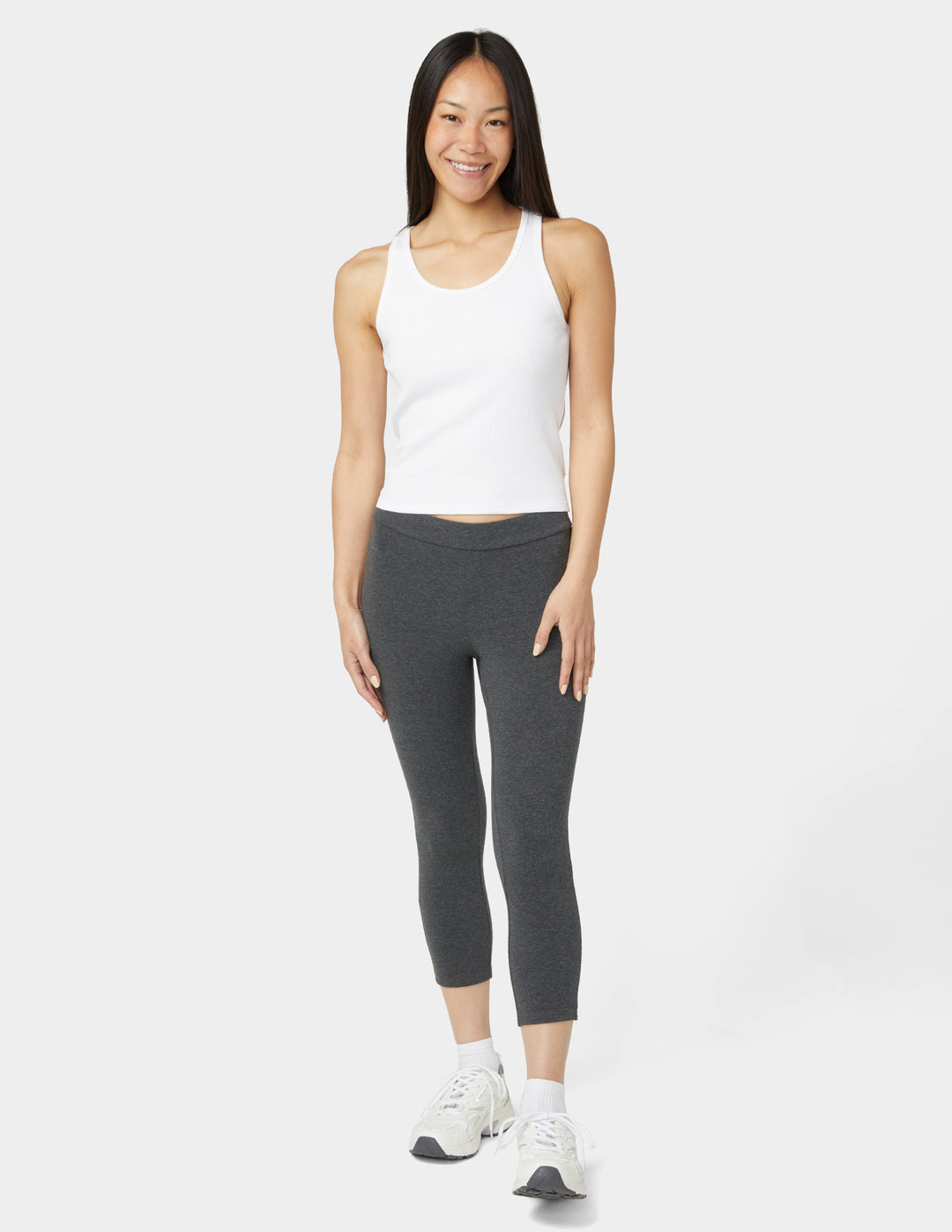 Woman wearing a white tank top and gray leggings on a white background