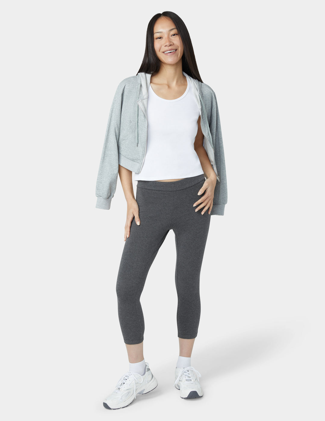 Woman wearing a gray jacket, white shirt, and dark gray leggings on a white background