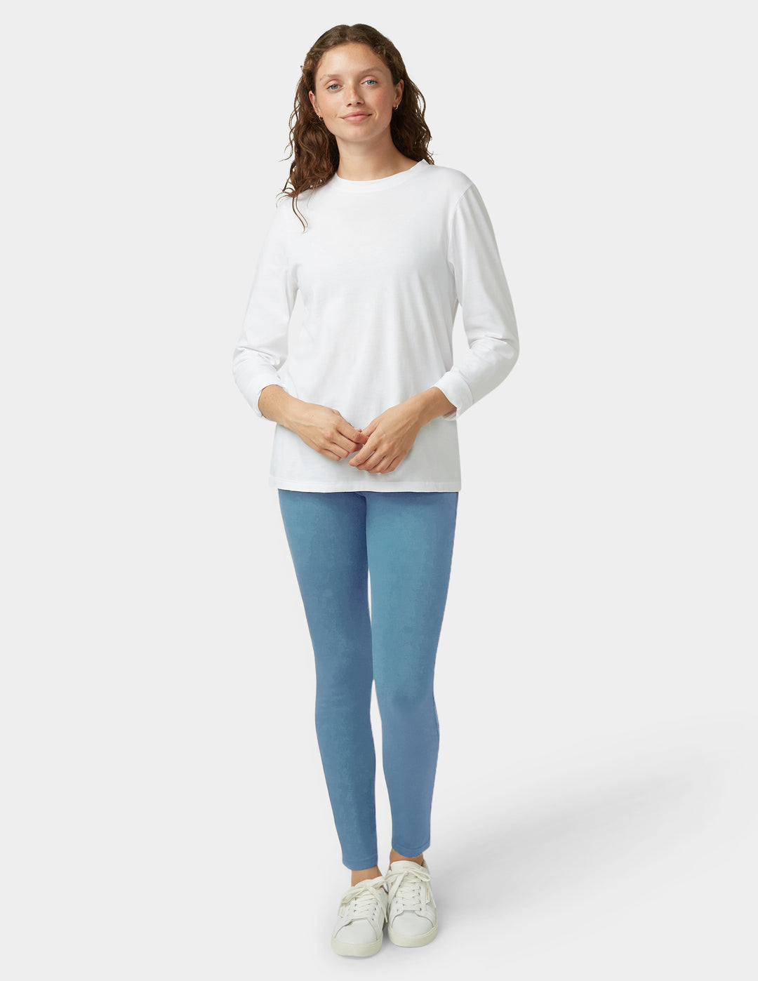 Woman wearing a white long-sleeve top and light blue leggings on a white background