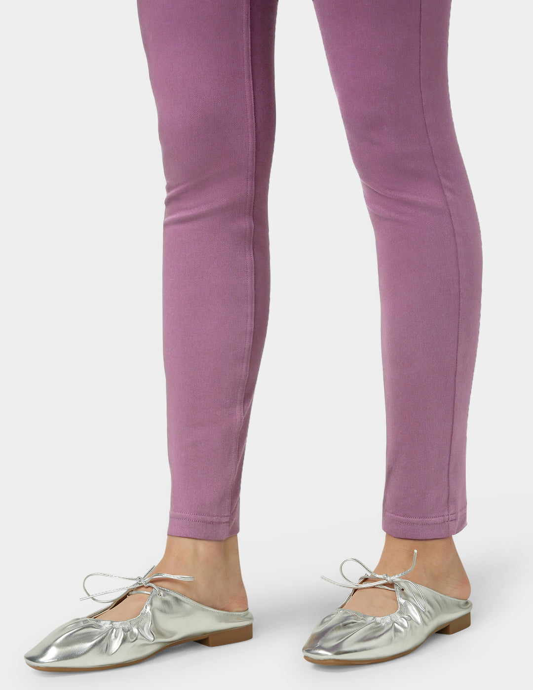 Purple leggings worn by a person with silver flats on a white background