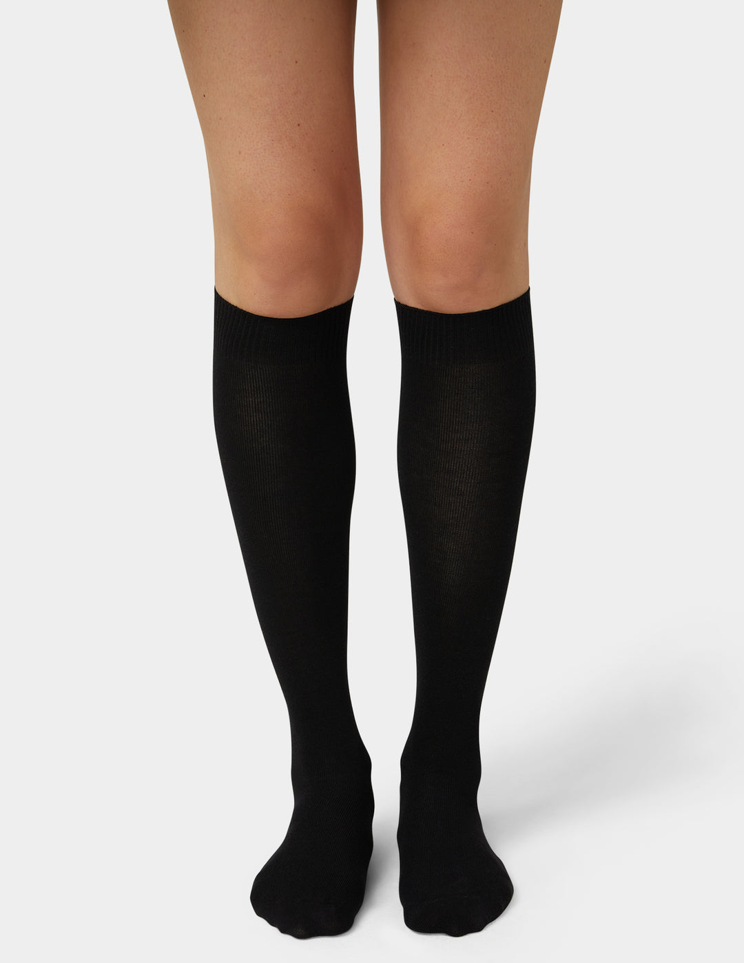 A pair of black knee-high compression socks worn on a model's legs, shown against a plain light gray studio background.