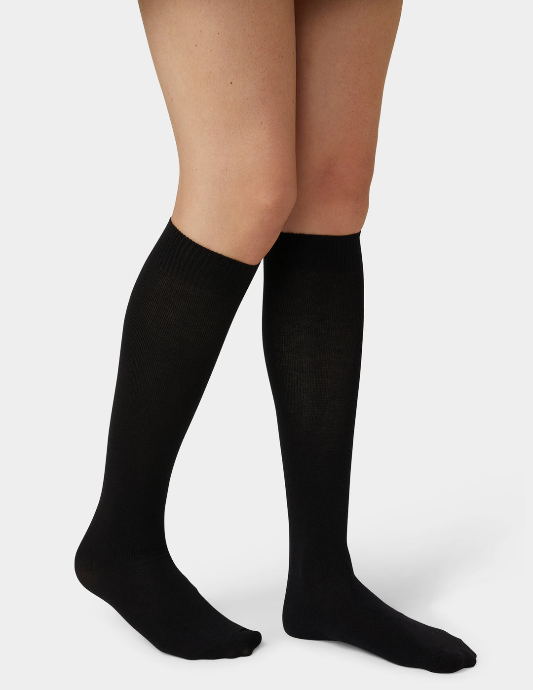 A pair of black knee-high socks worn on a model's legs, shown against a plain light gray studio background.