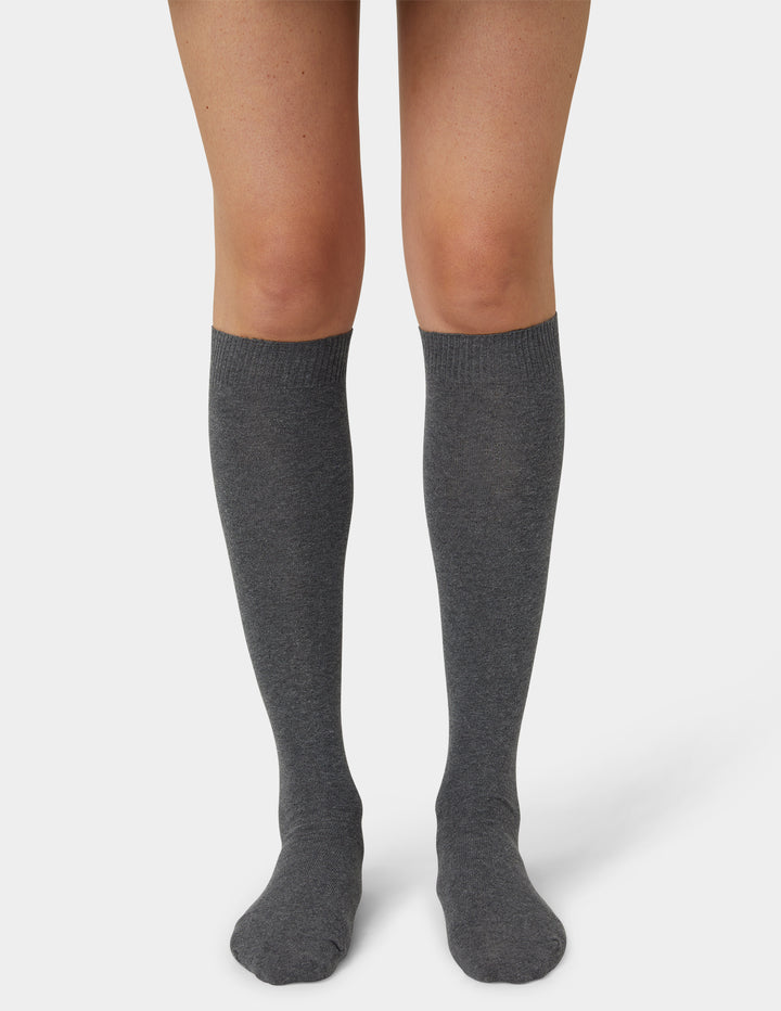 A pair of dark gray heathered knee-high socks worn on a model's legs, shown against a light gray studio background.