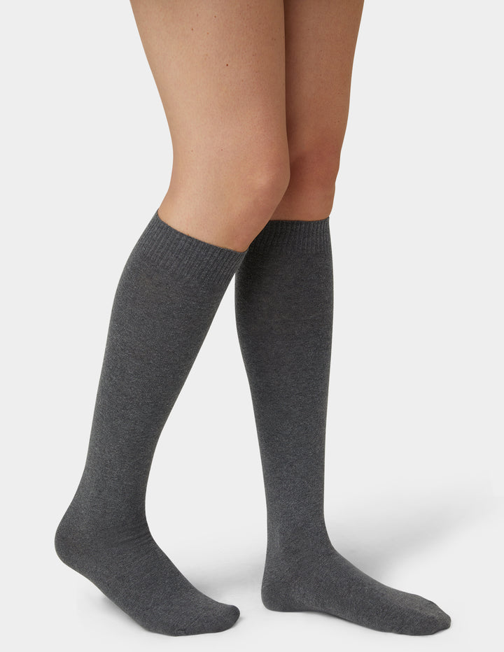 A pair of dark gray heathered knee-high socks worn on a model's legs, shown against a clean light gray studio background.