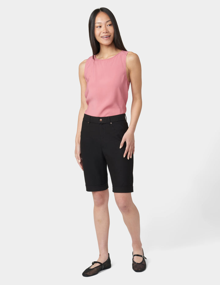 Woman wearing a pink sleeveless top and black shorts on a white background