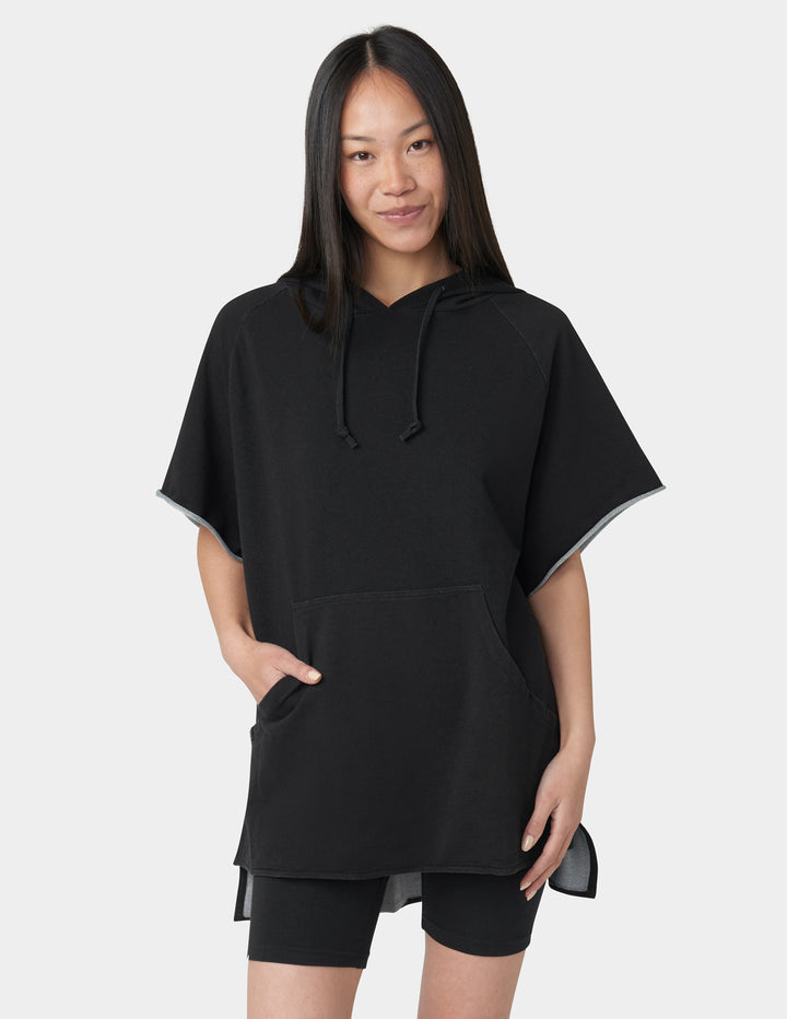Woman wearing a black poncho-style hoodie on a white background