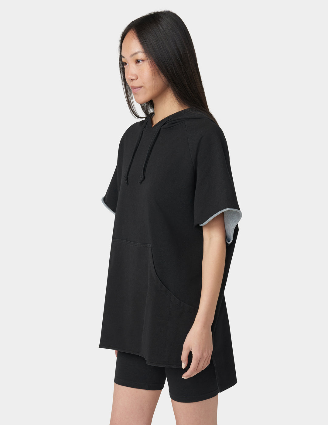 Person wearing a black oversized hoodie and shorts on a white background