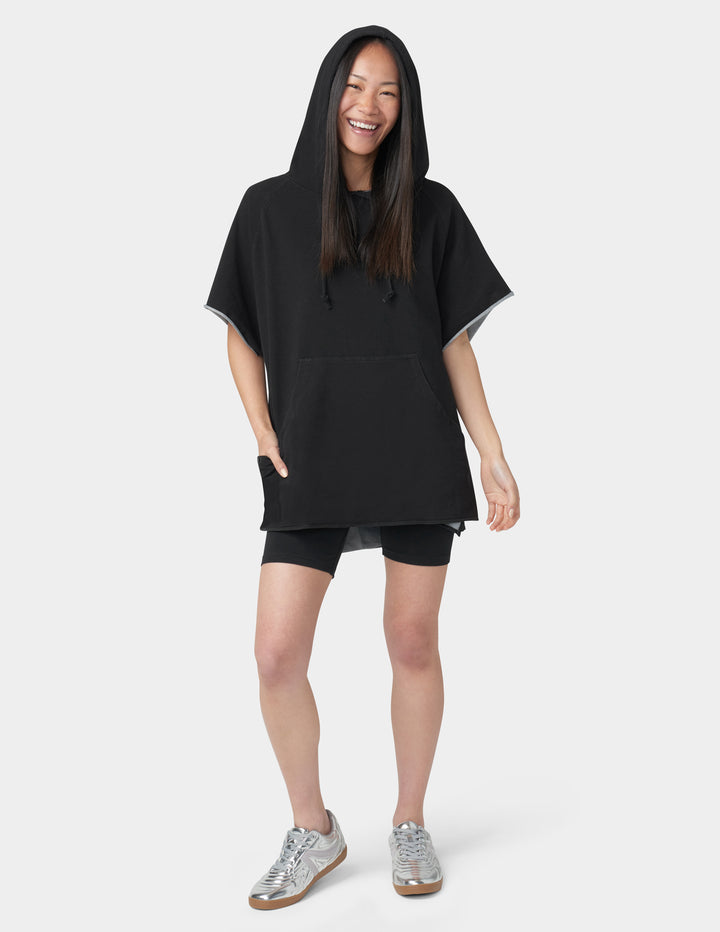 Person wearing a black hooded poncho over a black outfit on a white background