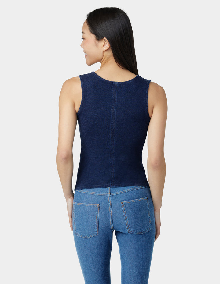 Woman wearing a navy blue sleeveless top and blue jeans on a white background