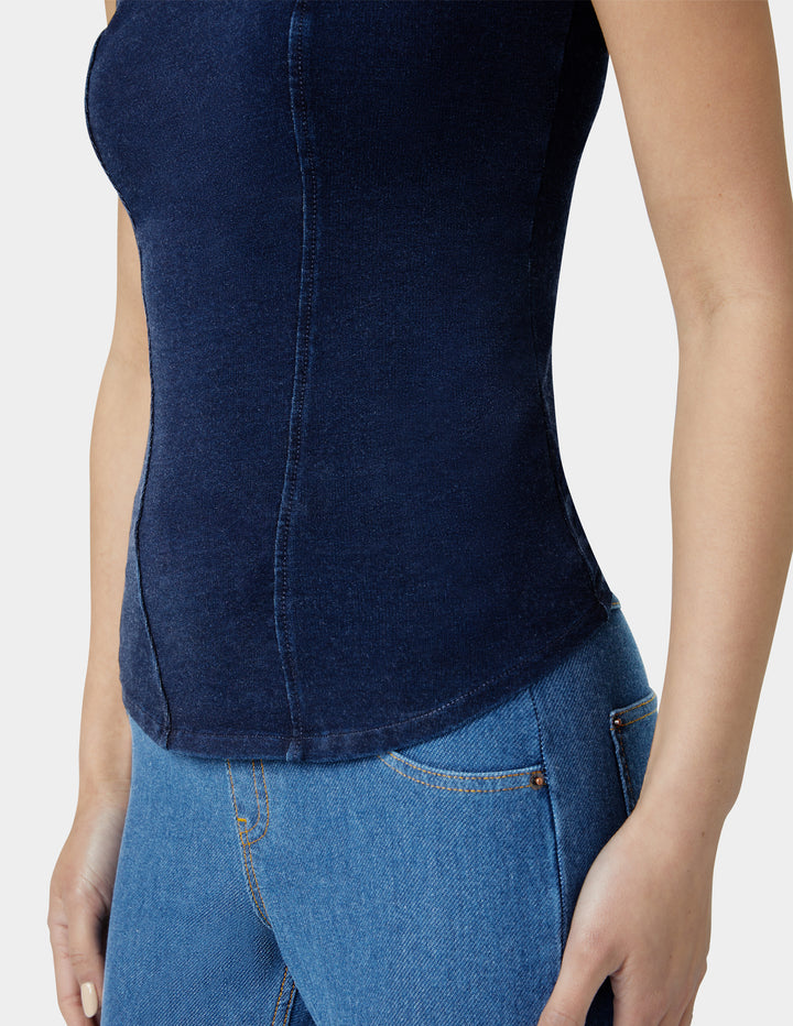 Person wearing a dark blue sleeveless top and jeans on a light gray background