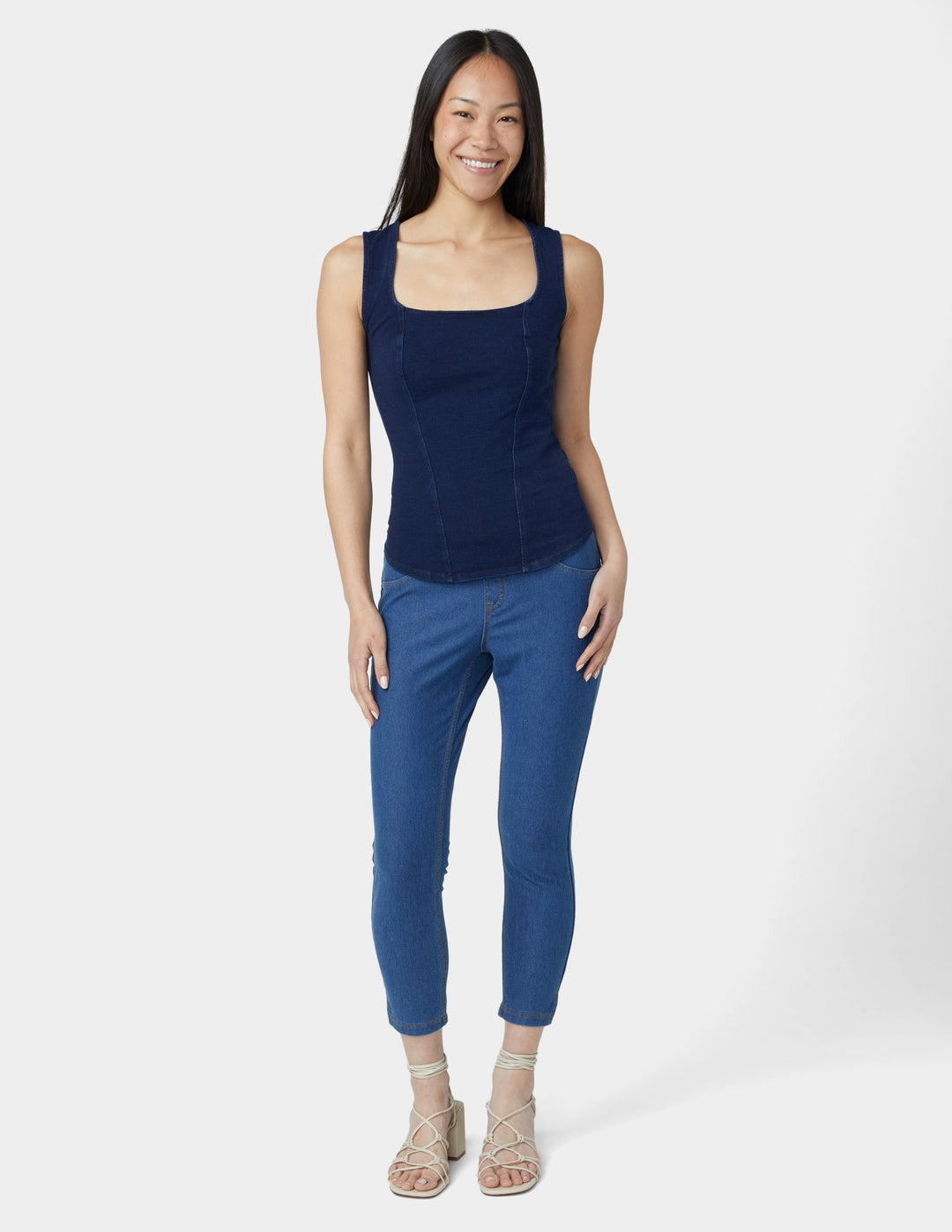 Woman wearing a navy sleeveless top and blue pants on a white background