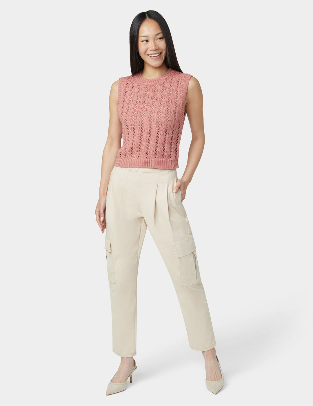 Woman wearing a pink sleeveless knitted top and beige cargo pants on a white background