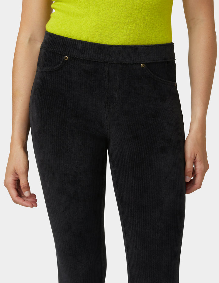 Black corduroy pants worn by a person with a green top on a white background