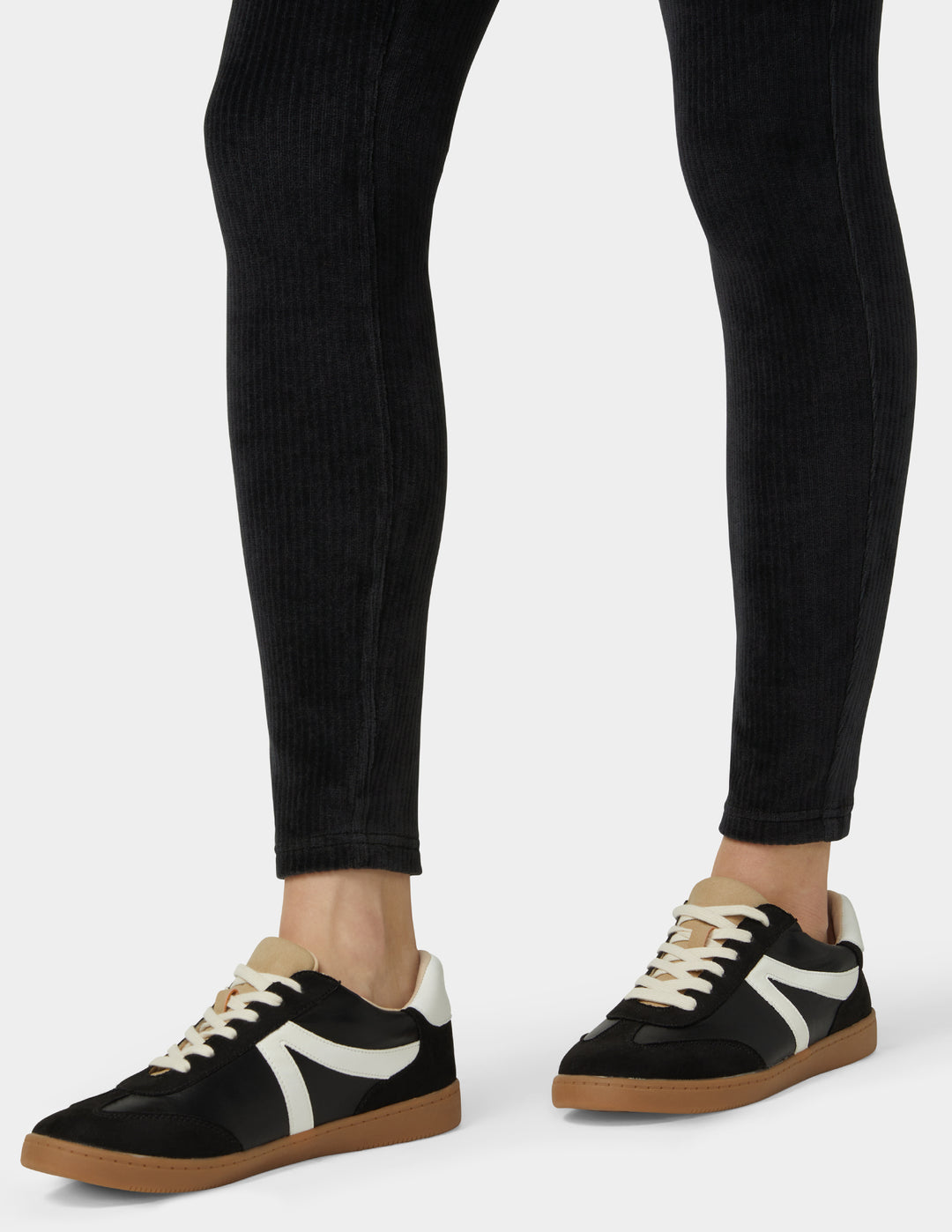 Black sneakers with white accents worn with black pants on a white background