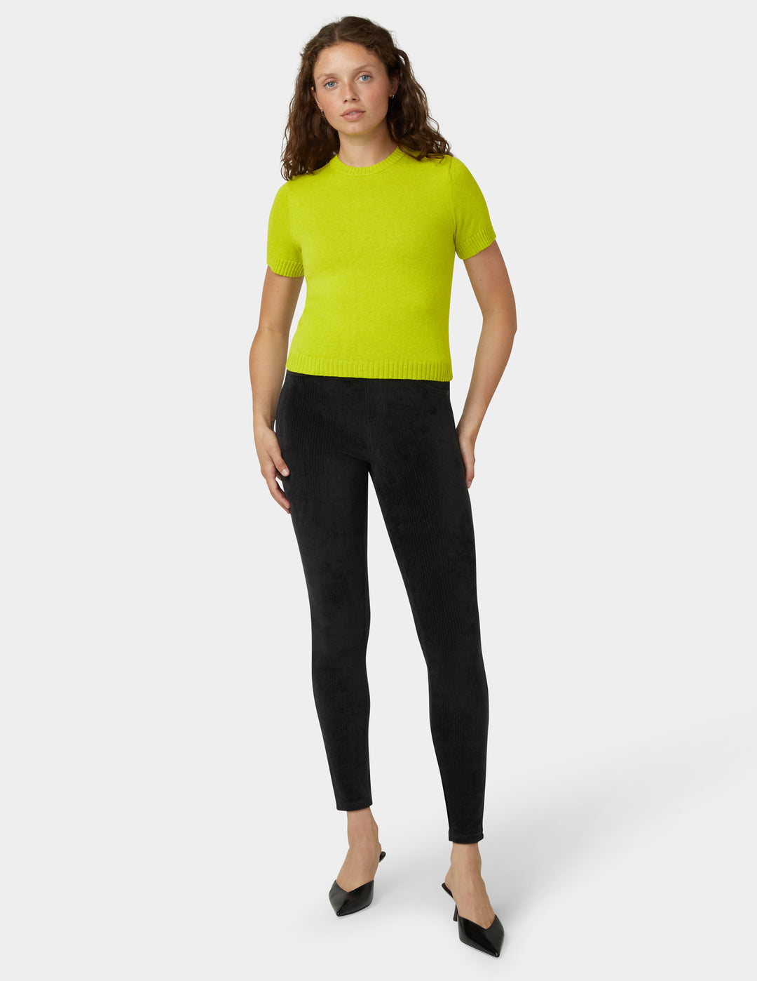 Woman wearing a bright green sweater and black pants on a white background