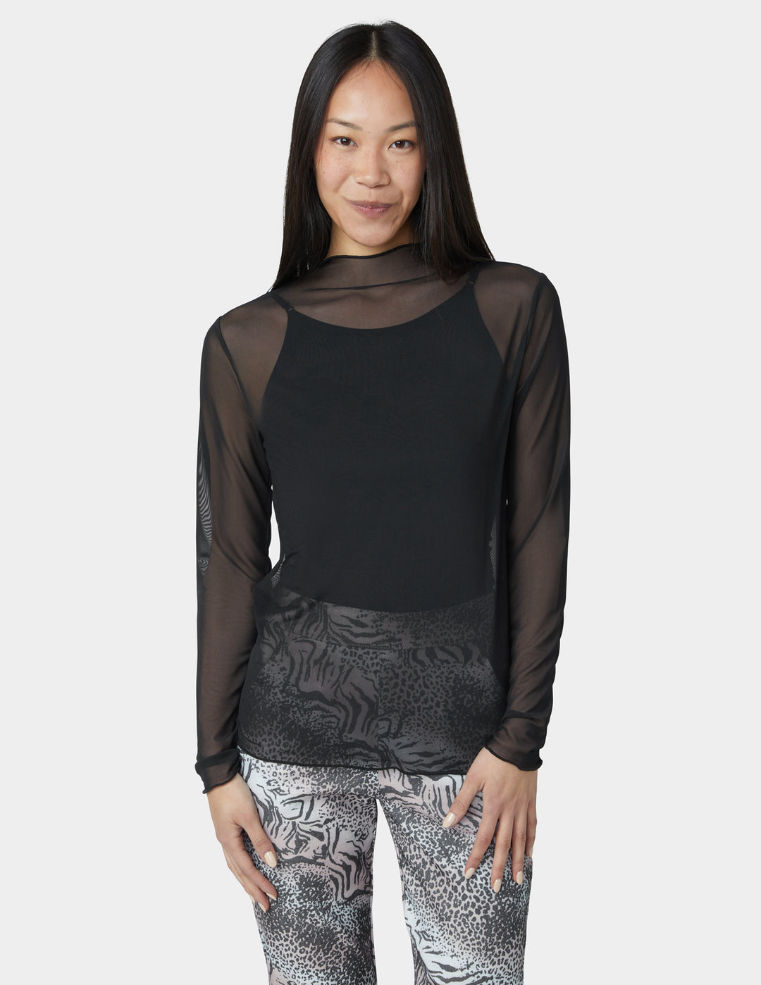 Woman wearing a black sheer top and patterned leggings on a white background