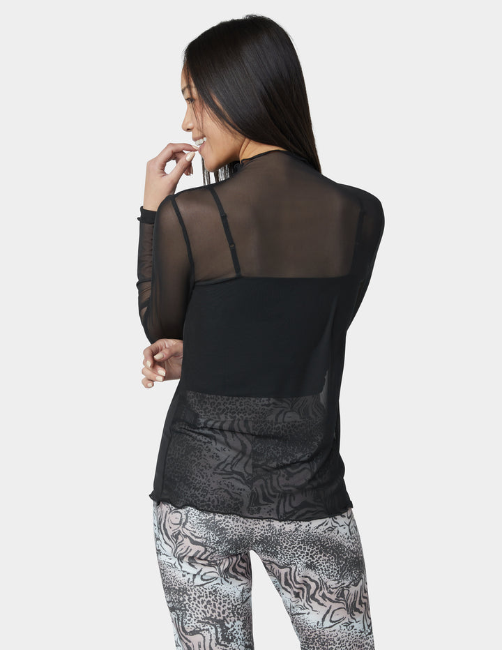 Woman wearing a black sheer top with patterned leggings on a white background